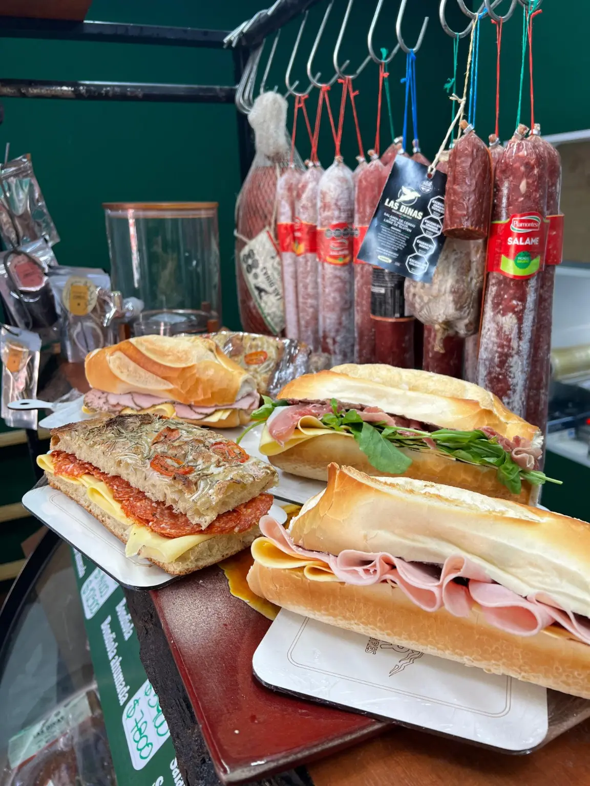 Sándwiches preparados en el mostrador de Del Sur, rodeados de fiambres